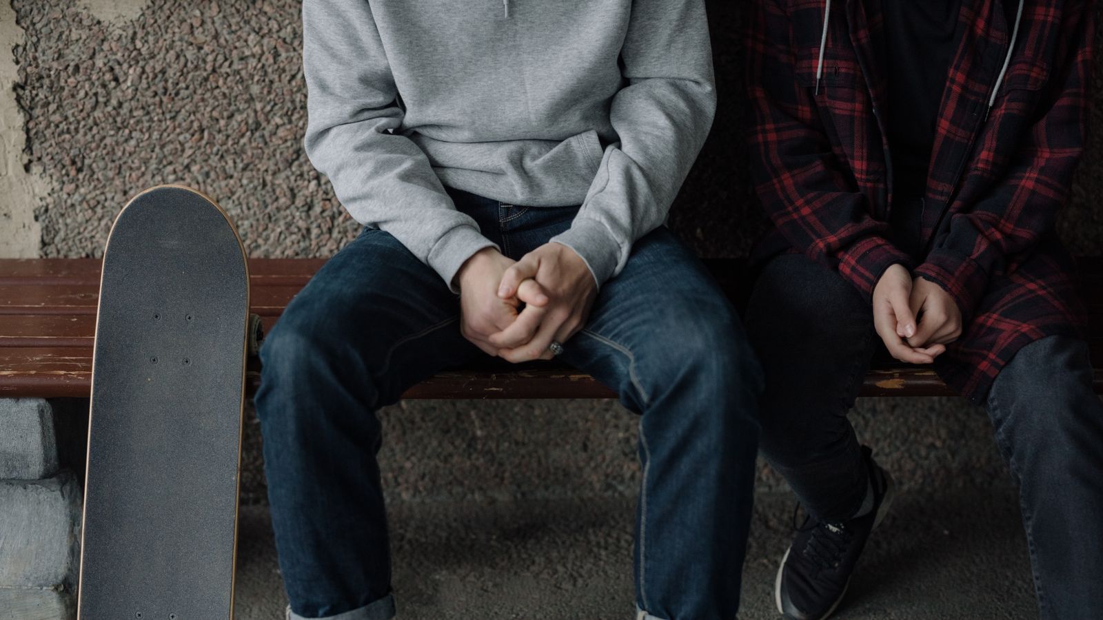 Two teenagers sit casually on a bench with a skateboard, embodying youthful skate culture.