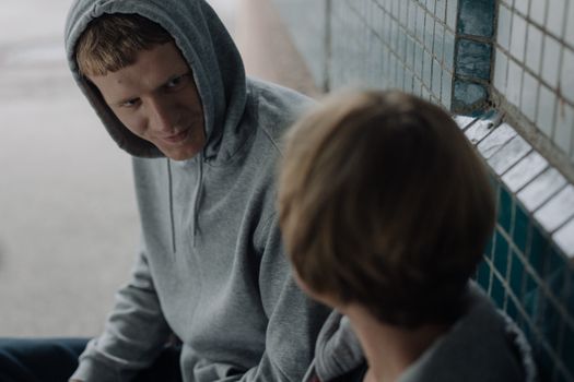 Two people in gray hoodies sharing a moment in an urban tiled space.