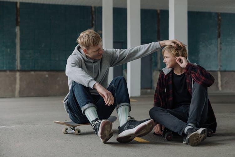 Brothers Sitting On Skateboards Talking