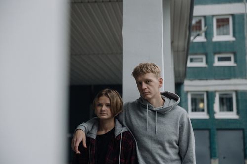 Free Two siblings in casual wear leaning against a pillar, showcasing a relaxed urban vibe. Stock Photo