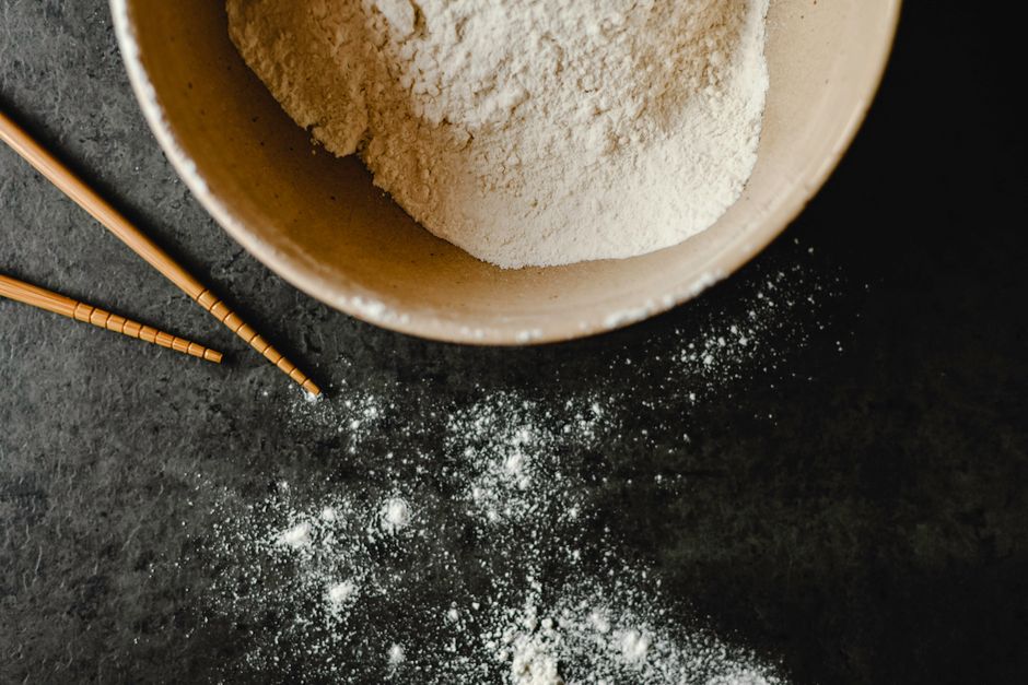 Close-up of flour in a beige bowl with chopsticks on a dark background. Ideal for food photography.