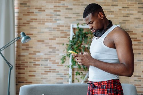 Free Casual young man using smartphone at home, wearing headphones. Stock Photo