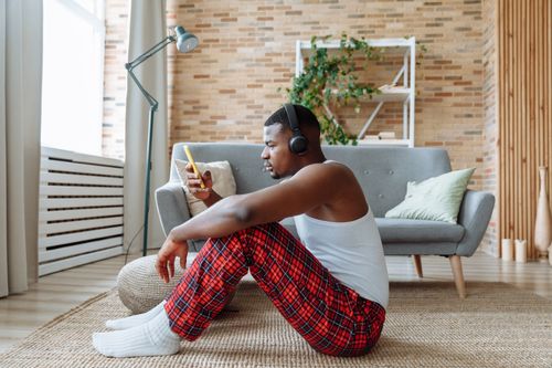Free Man in plaid pajamas with headphones enjoys music on smartphone indoors. Stock Photo
