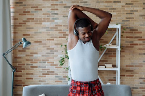 Free Man in a White Tank Top Stretching while Listening to Music Stock Photo
