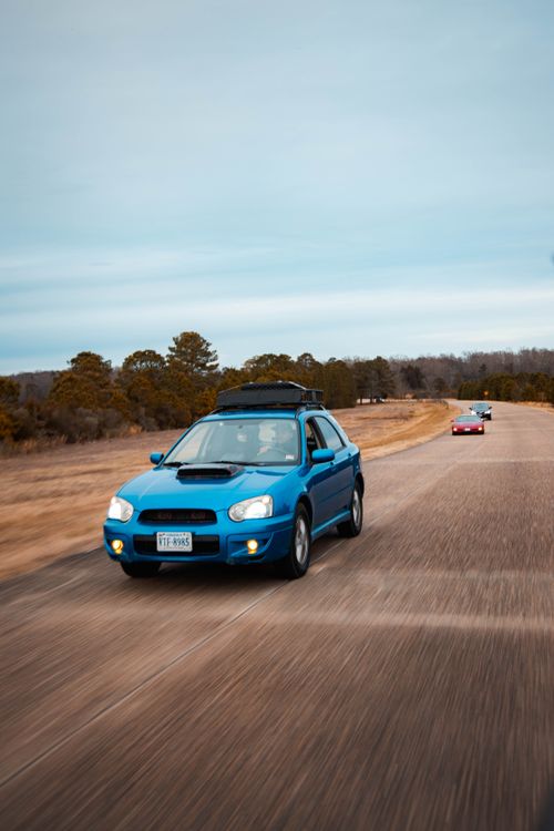 Free A blue sports car speeds down an open road, capturing the thrill of driving. Stock Photo