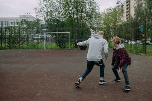 Two teenagers playing basketball on an outdoor court in an urban setting.