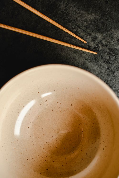 Free Top view of an empty ceramic bowl and chopsticks on a textured dark surface, creating a minimalist aesthetic. Stock Photo