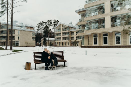 A senior couple sitting on a bench amid snow-covered modern apartments.