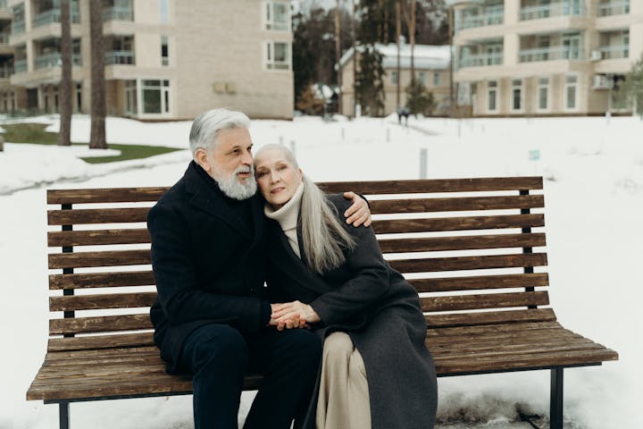 Elderly couple embracing on a bench in a snowy outdoor setting, showcasing love and togetherness.