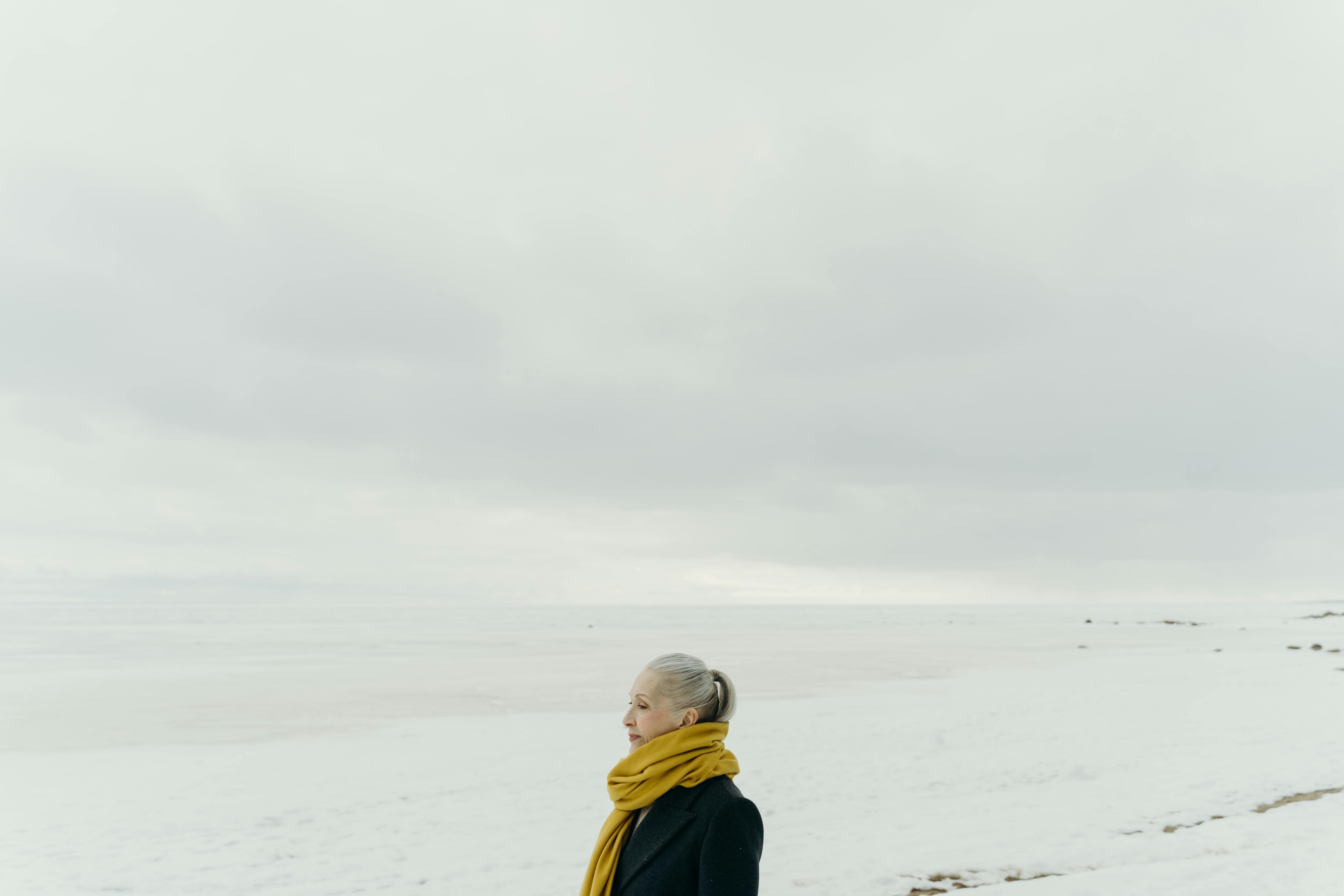 Senior woman with yellow scarf in snowy landscape, showcasing winter elegance.