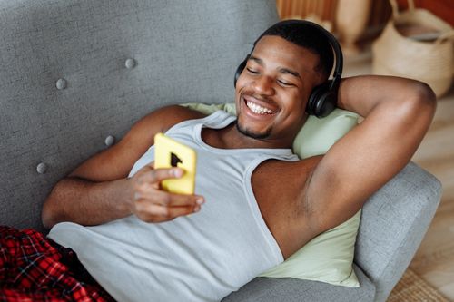 Free Happy man enjoying a video call while relaxing comfortably on a couch with headphones. Stock Photo