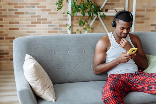 Free Adult man enjoying music on headphones while using his phone in a cozy living room. Stock Photo