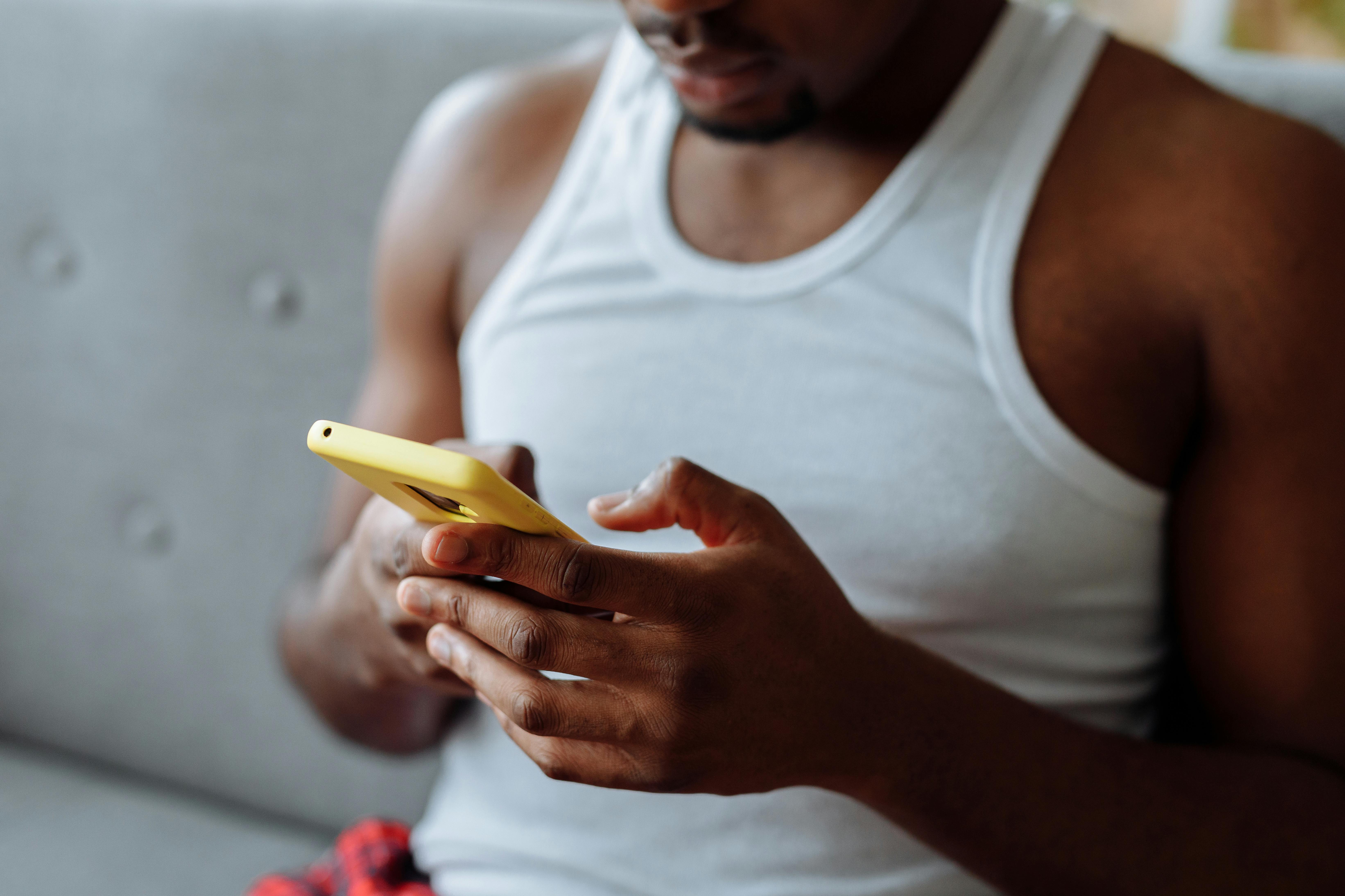 Adult man using a yellow smartphone while seated indoors on a couch.