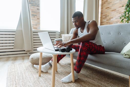 A young man in casual wear typing on a laptop while sitting on a sofa indoors.