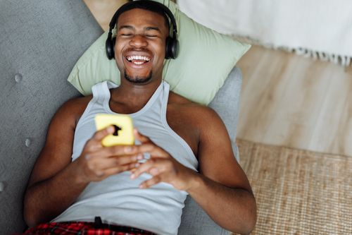 Free Young man enjoying music on headphones while lounging on the sofa with a smartphone. Stock Photo