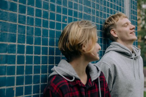 Free Two young adults smiling and enjoying a moment against a blue tiled wall. Stock Photo