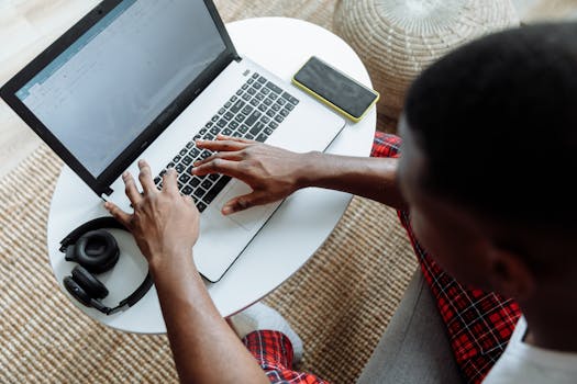 Top view of a man typing on a laptop, with a smartphone and headphones on the desk.