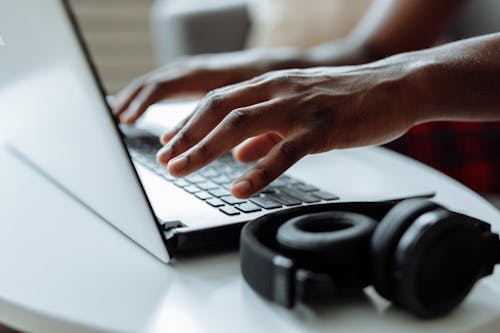 Close-Up Photograph of a Person's Hands Typing on a Laptop Beside Headphones   