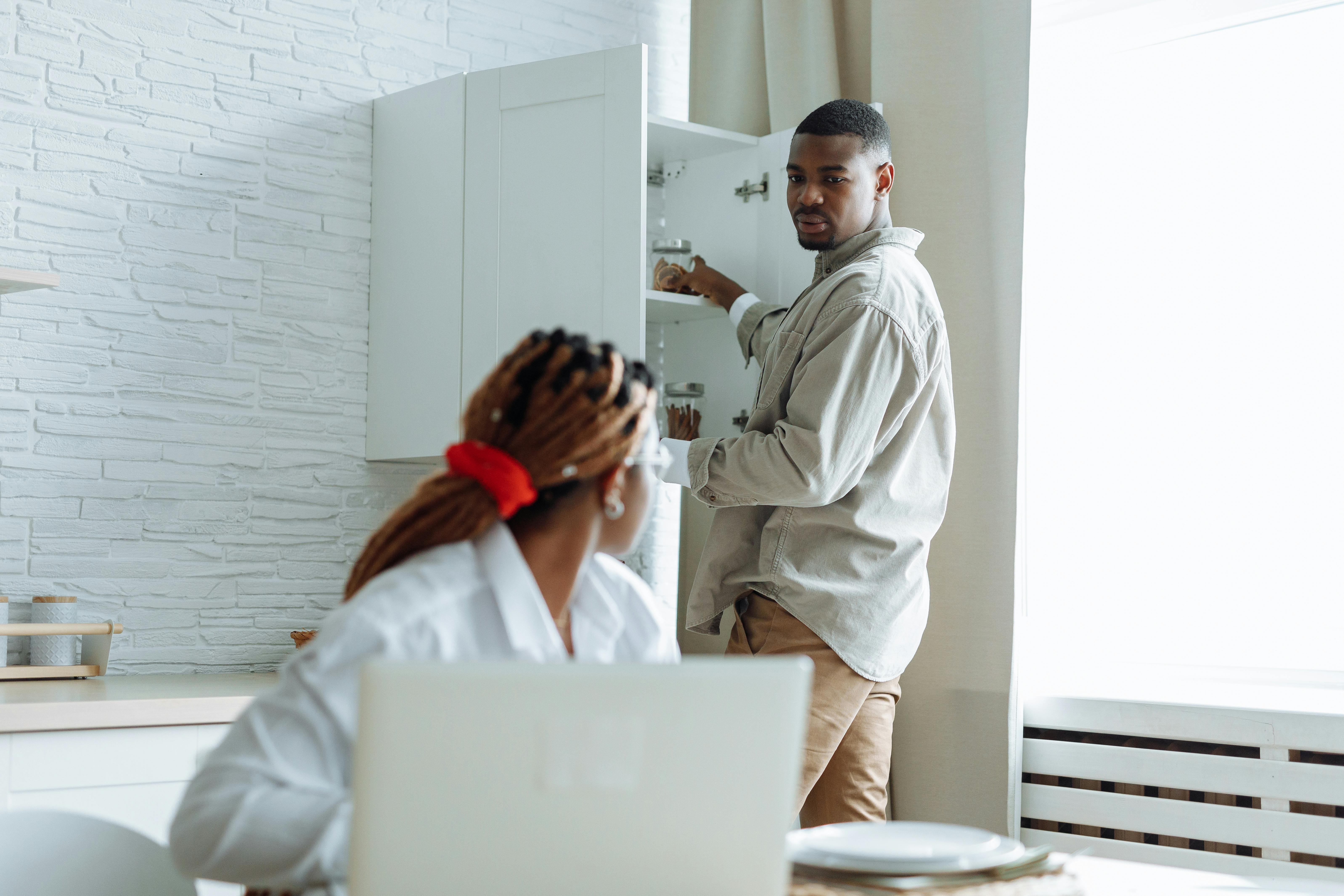 A couple interacting in a modern kitchen with laptop and open cupboard, capturing a warm home scene.