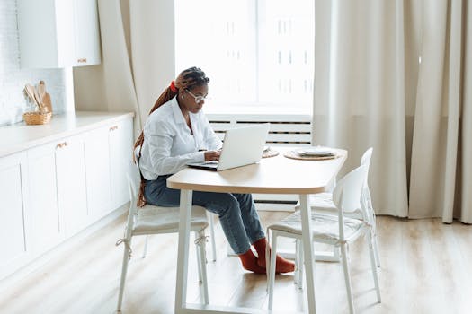 African American woman focused on remote work at home, using a laptop in a bright and modern kitchen.