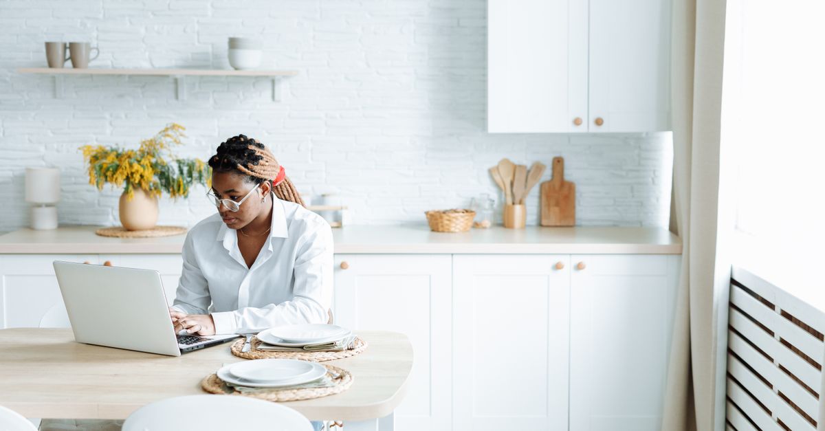 person typing on laptop at kitchen table