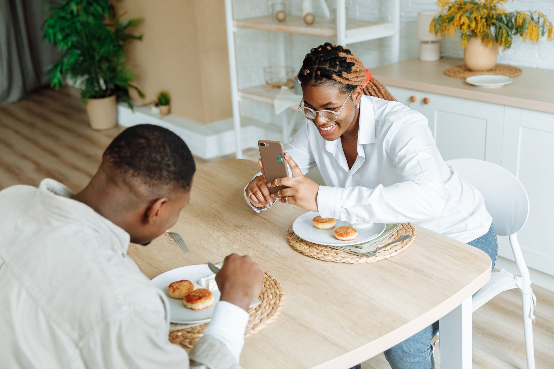 Casal sentado à mesa de jantar olhando a tela de um celular juntos para conferir gastos.