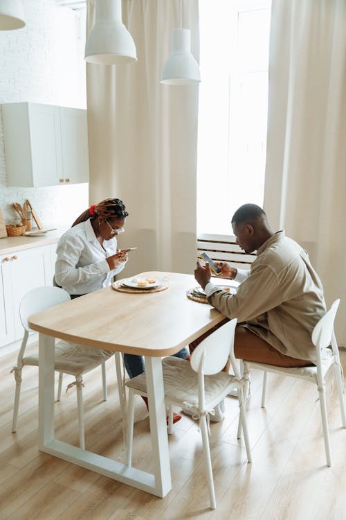 Man and Woman Sitting at the Table Having Breakfast and Using Cellphone