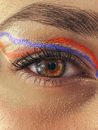 Closeup brown eye and eyebrow of anonymous female with bright purple and orange eyeliner with painted eyelashes looking at camera