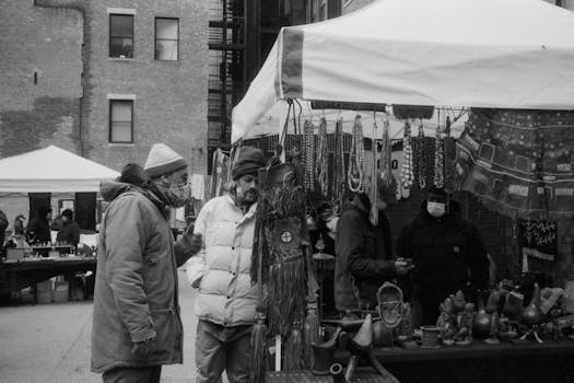 Monochrome image of a busy street market with vendors and shoppers in winter clothing.