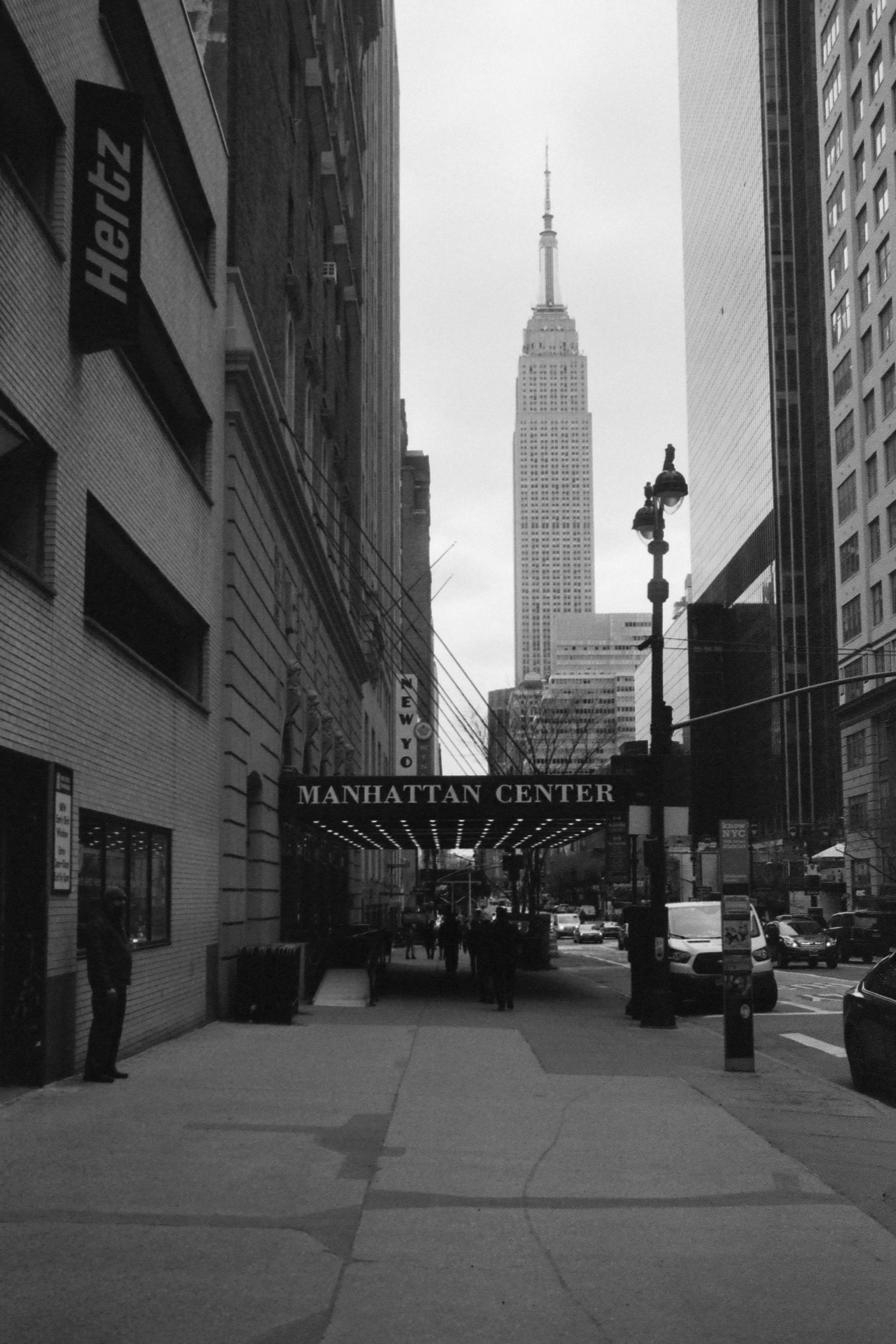 Grayscale urban scene featuring Manhattan Center with Empire State Building in the background.