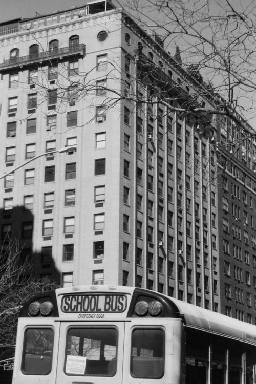 Free Grayscale image of a school bus next to a tall urban apartment building. Stock Photo