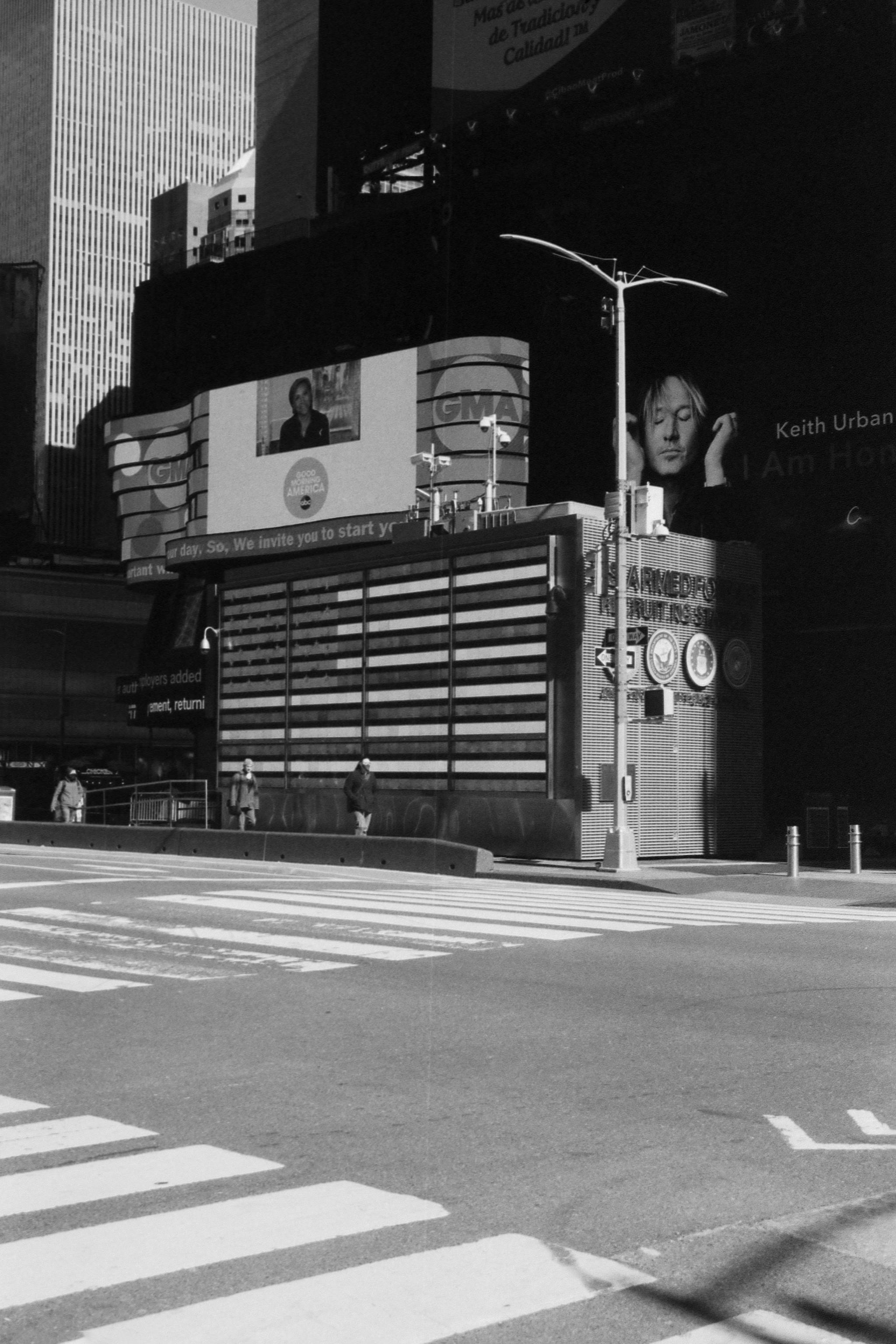 Monochrome street view of Times Square with billboards and zebra crossing.