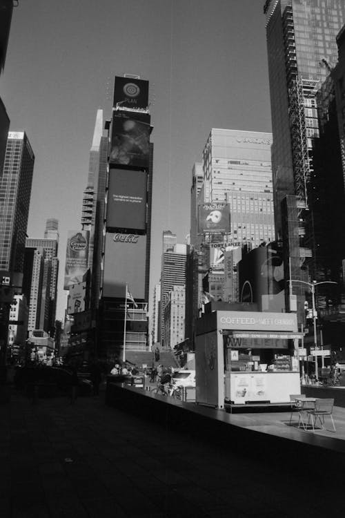 Grayscale Photo of Coffee Kiosk at the Plaza Near City Buildings 