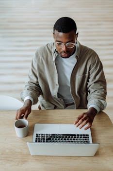 High angle view of a man working on a laptop with a coffee cup indoors, showcasing remote work lifestyle.