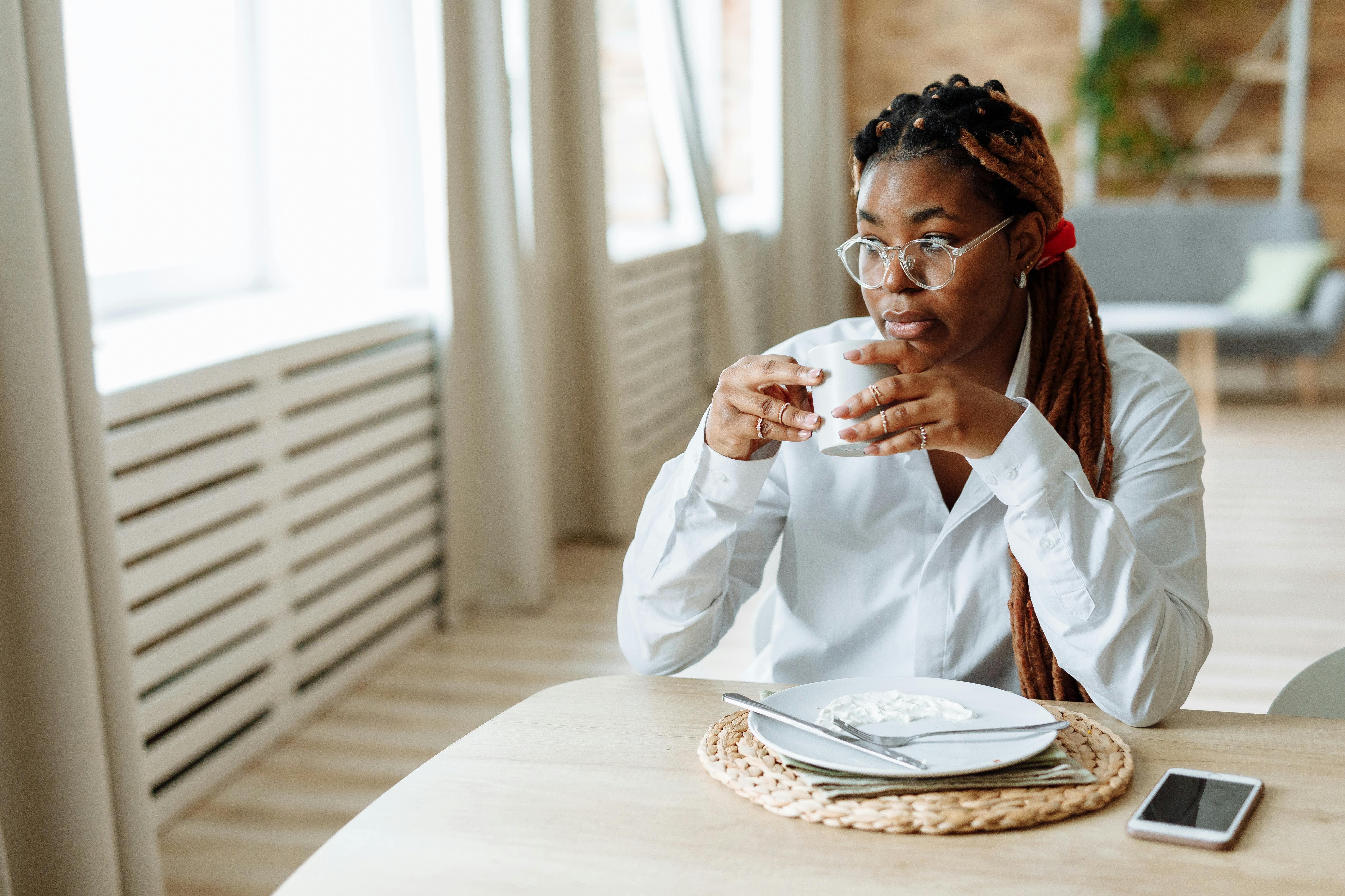 A professional woman in a colorful African print blouse drinking water by a window in Ho, Ghana, morning light