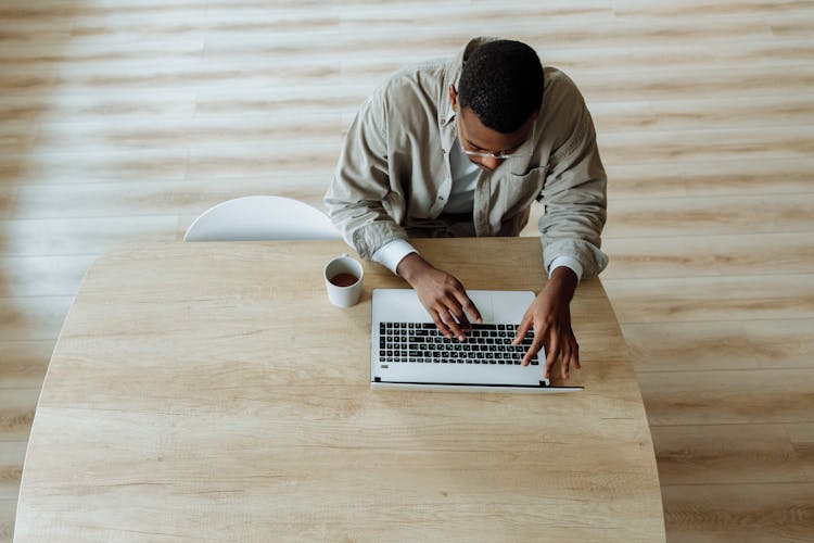 Overhead Shot Of A Man Working On His Laptop Near A Cup Of Coffee