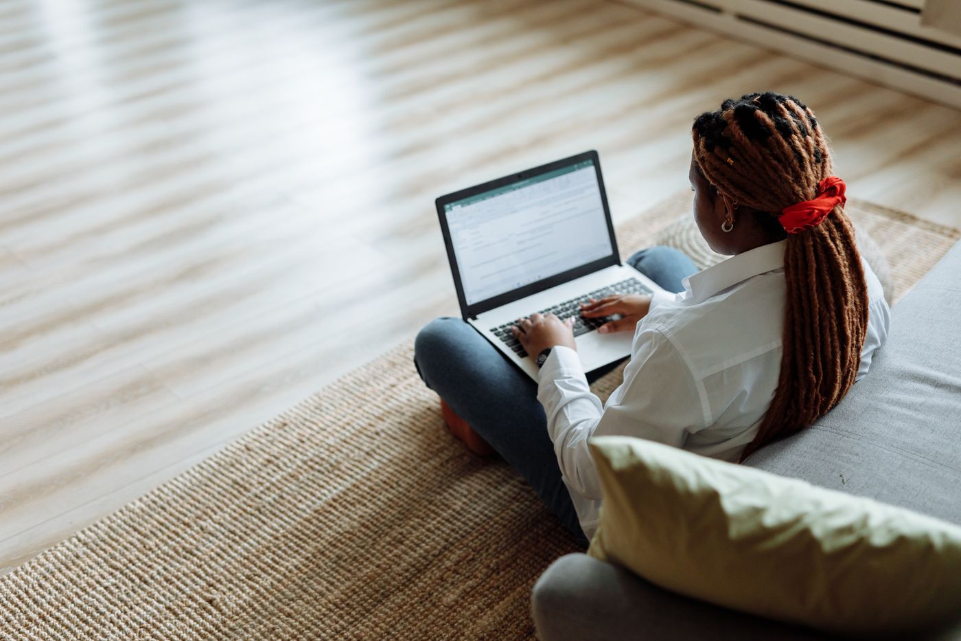 An African American woman with dreadlocks works on her laptop from the comfort of her home.