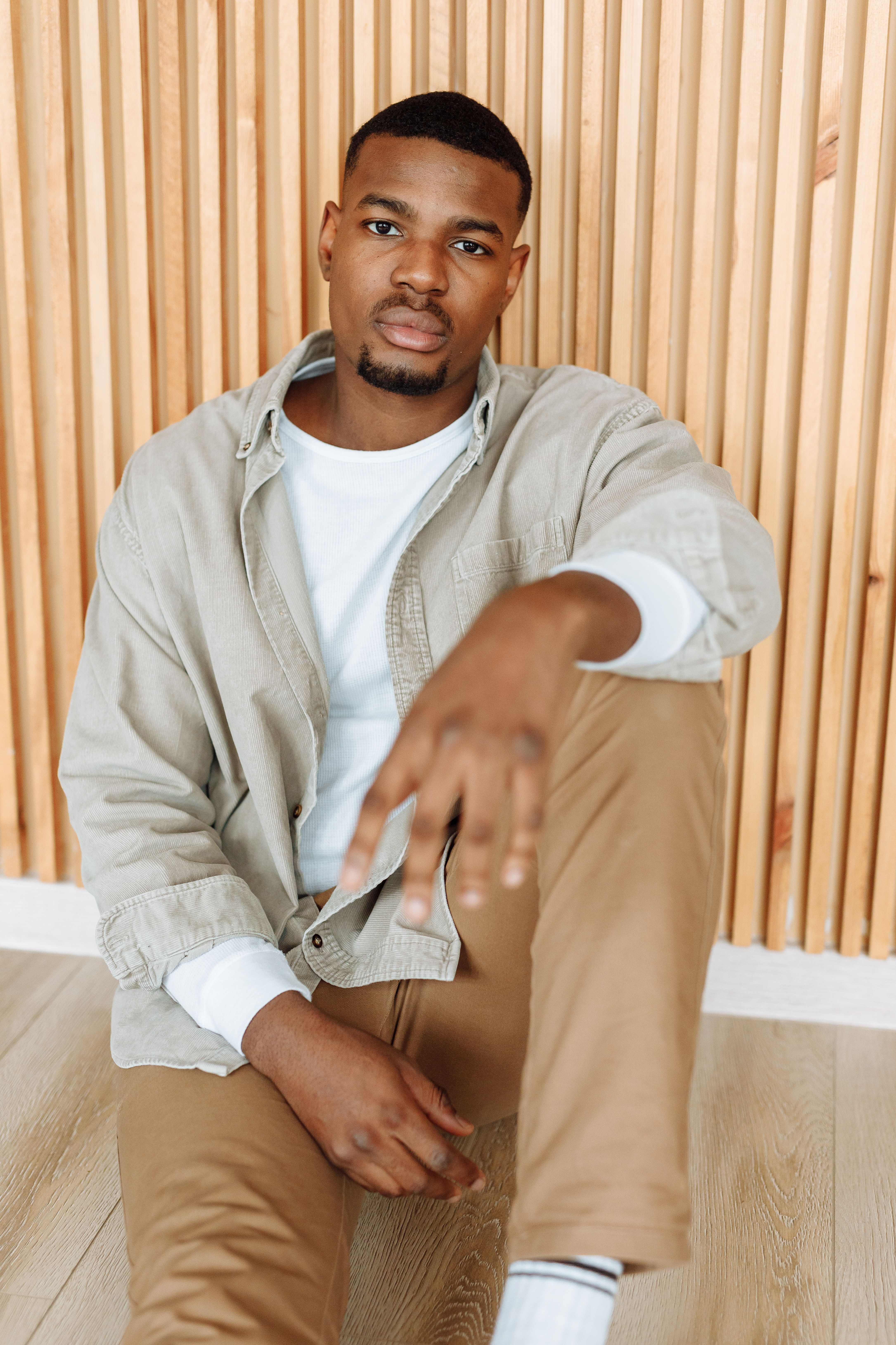 Fashionable African American man posing indoors against a wooden panel backdrop.