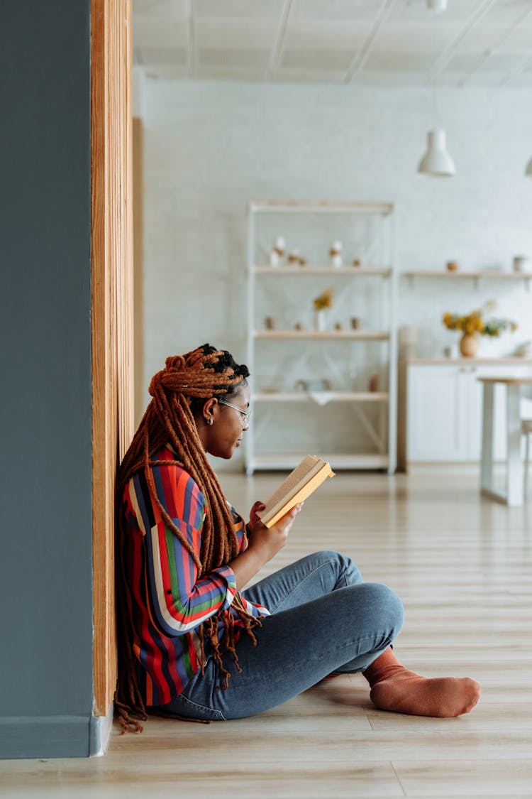 A Woman In Afro Braids Sitting On The Floor While Reading Book