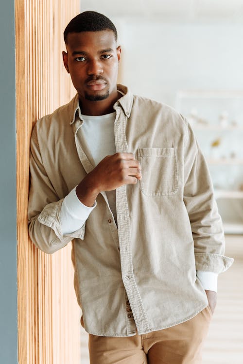 A Stylish Man Leaning on a Wooden Surface while Looking at the Camera