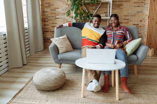 Photo of a Man and a Woman Sitting on a Sofa while Watching on a Laptop