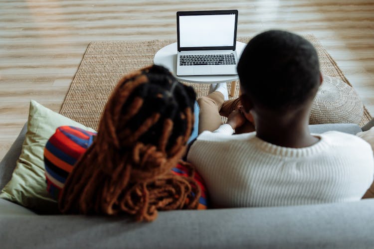 A Couple Sitting On A Couch In Front Of A Laptop With Blank Screen