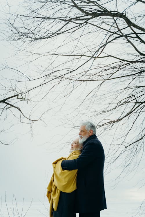Free Photo of an Elderly Couple Hugging Under a Leafless Tree Stock Photo