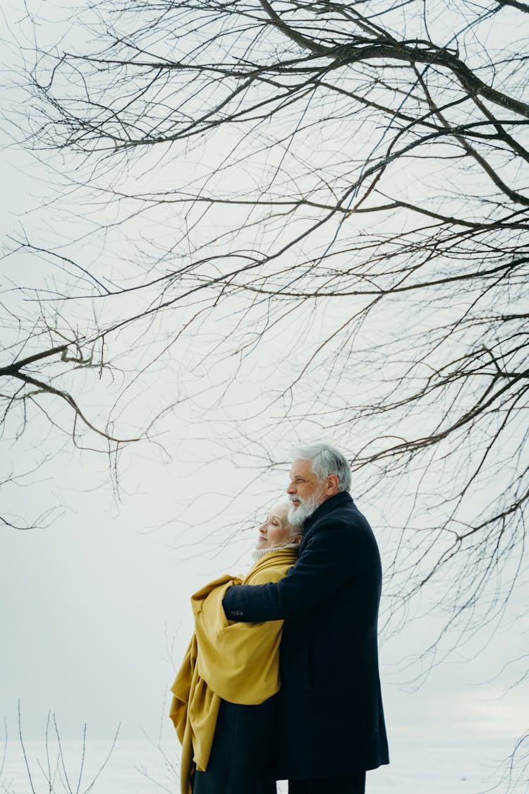 Photo Of An Elderly Couple Hugging Under A Leafless Tree