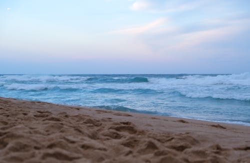 Photograph of a Beach with Brown Sand Near a Sea with Waves