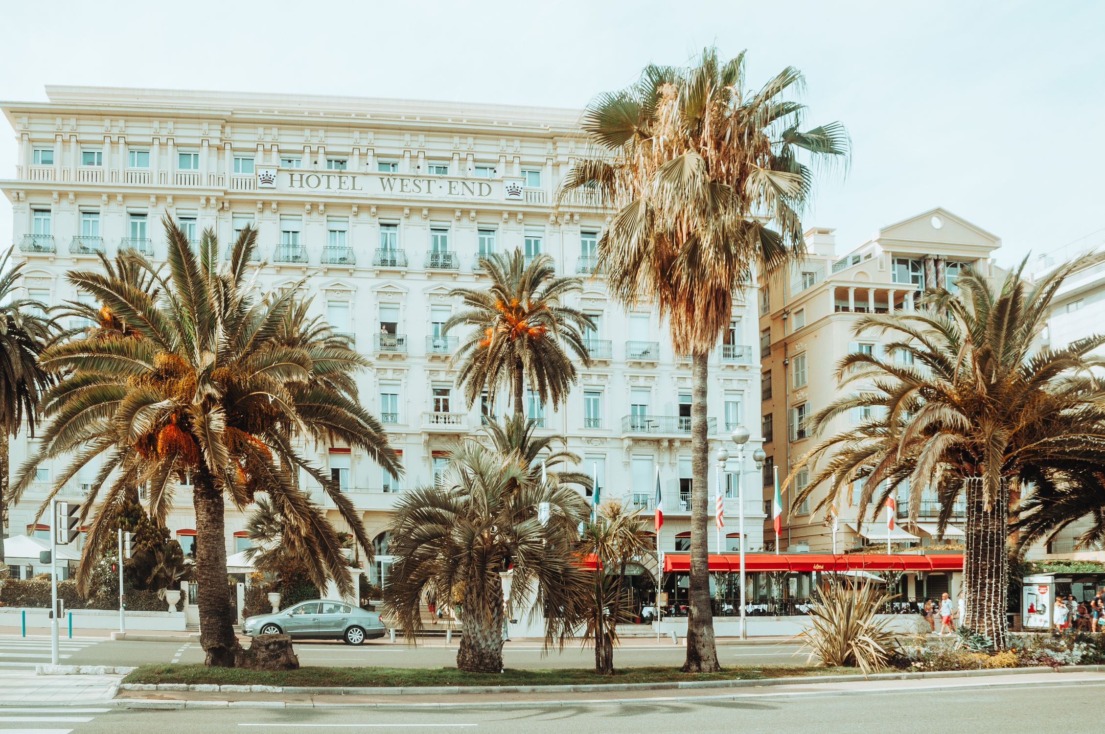 A palm-lined street near the seafront hotels of Nice, France under a clear sky.