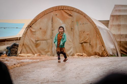 Free A young girl in a green jacket walks in a refugee camp in Idlib, Syria. Stock Photo