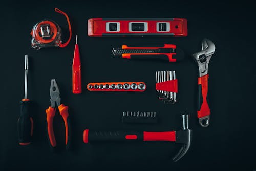 Top view arrangement of various repair tools including pliers hammer screwdriver and tape measure placed on black table