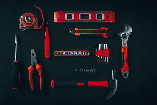 Top view arrangement of various repair tools including pliers hammer screwdriver and tape measure placed on black table