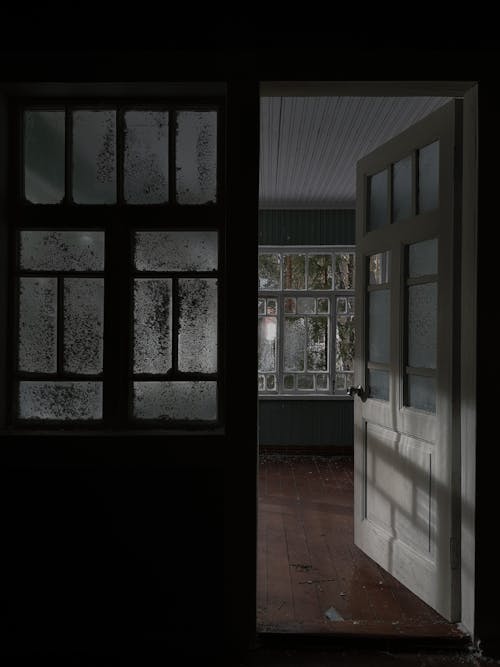 Opened door leading to empty light room with large windows placed in house in daytime